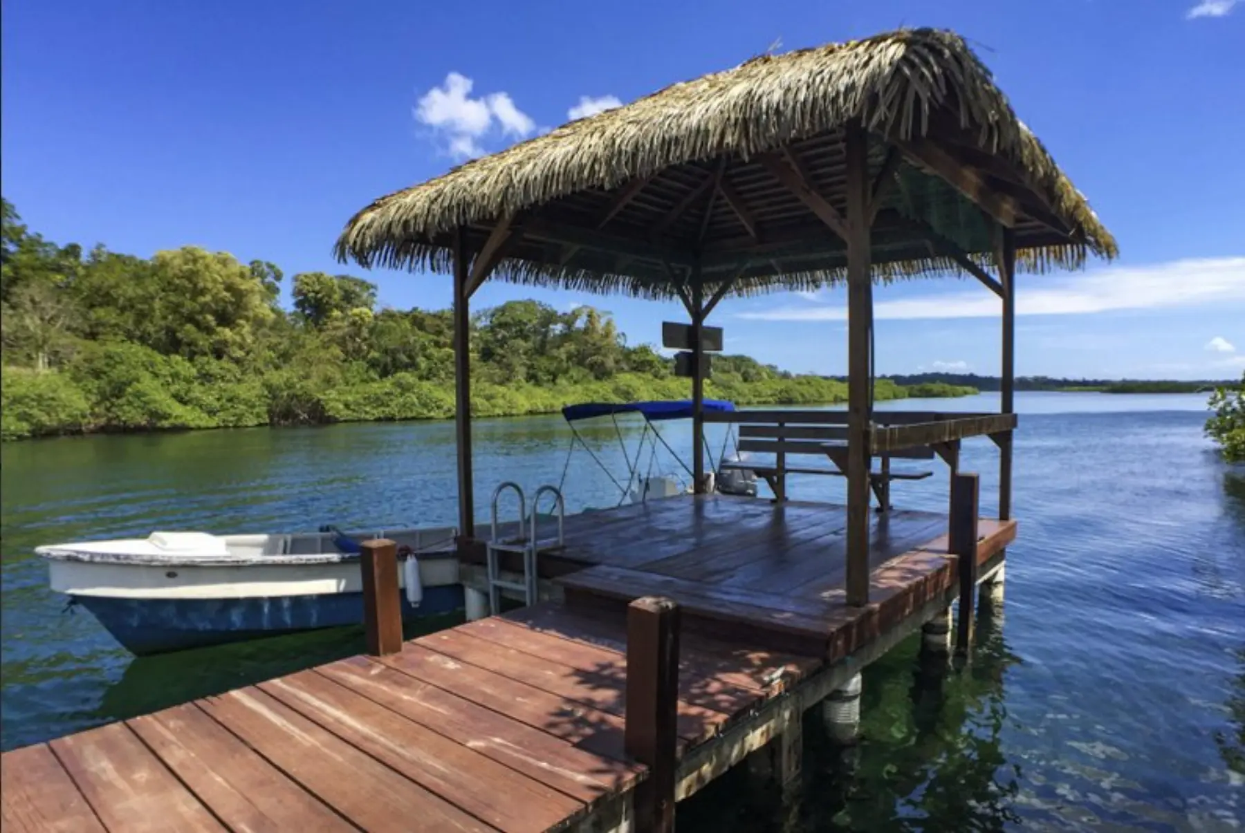 The thatched-roof boat house at the dock, with a small boat tied up and clear water