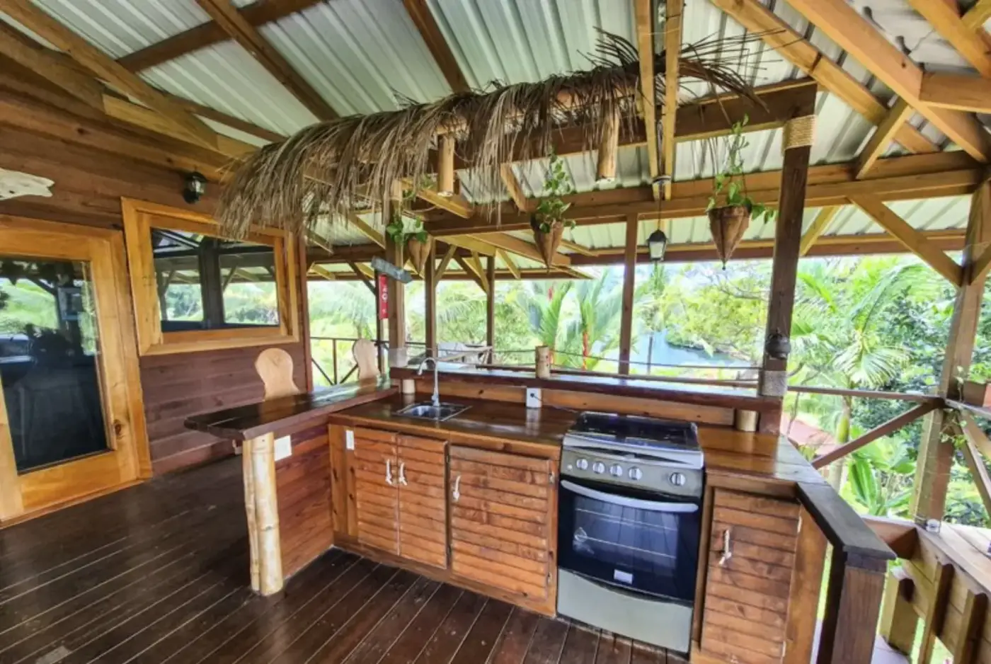 The main kitchen with thatched palm overhang, granite counters, and a view through to the water